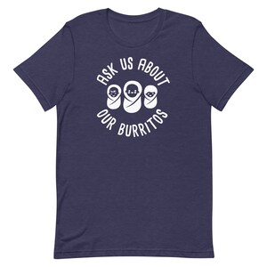 Puede incluir: Una camiseta azul marino con un dise&ntilde;o circular blanco que dice "Ask Us About Our Burritos" con tres caras de beb&eacute;s dentro del c&iacute;rculo.