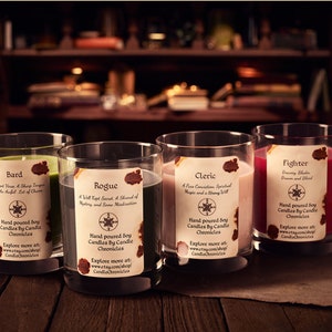May include: Four soy candles in clear glass tumblers, each with a different color wax: green, gray, pink, and red. Each candle has a label with a title and description. The candles are on a wooden surface.