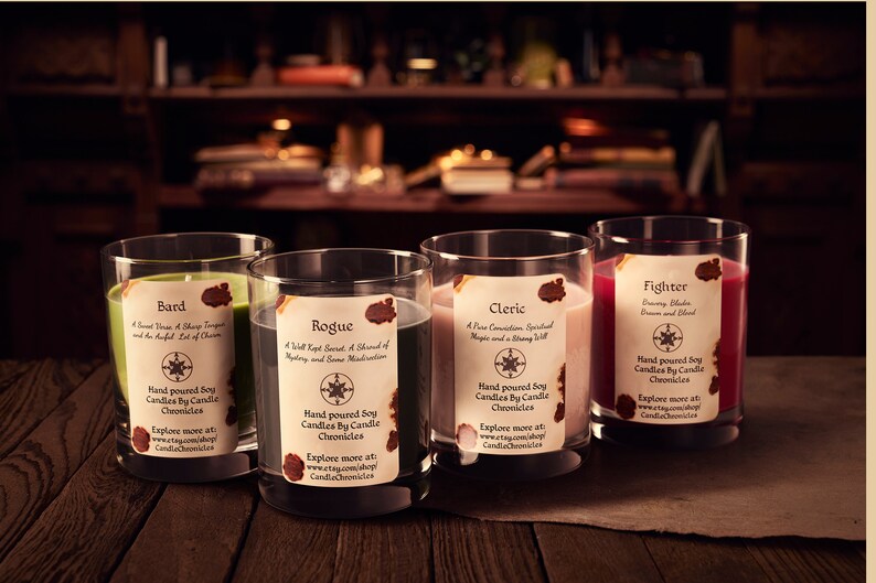 May include: Four soy candles in clear glass tumblers, each with a different color wax: green, gray, pink, and red. Each candle has a label with a title and description. The candles are on a wooden surface.