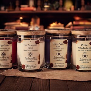 May include: Four soy candles in glass jars with wooden lids. Each candle has a label with a unique name: "Sandy Claws," "The Pumpkin King," "Three Wise Men," and "Winter Wonderland." The labels feature a compass rose design and the words "Candle Chronicles."