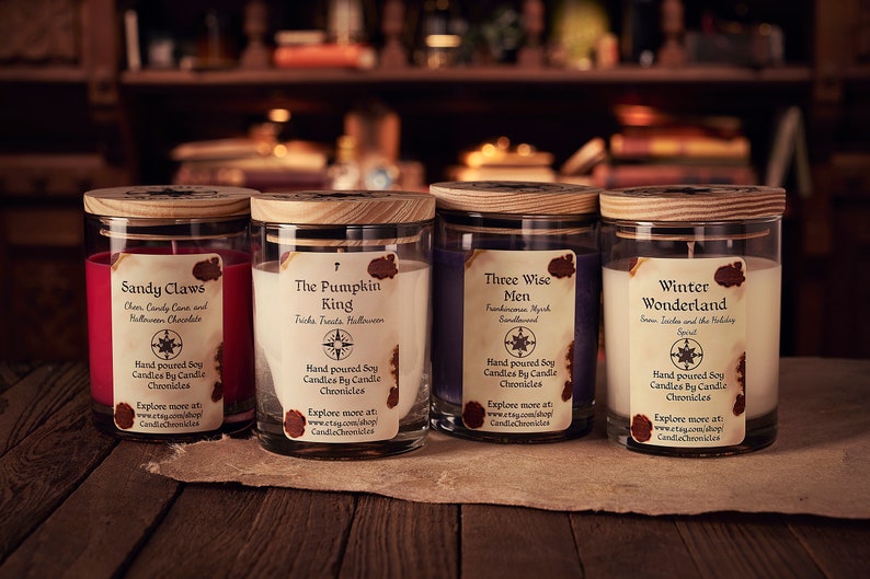 May include: Four soy candles in glass jars with wooden lids. Each candle has a label with a unique name: "Sandy Claws," "The Pumpkin King," "Three Wise Men," and "Winter Wonderland." The labels feature a compass rose design and the words "Candle Chronicles."
