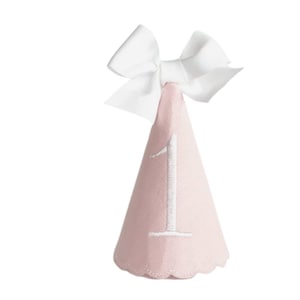 May include: A light pink party hat with a white bow at the top. The number "1" is embroidered in white on the front of the cone-shaped hat. The bottom edge of the hat has a scalloped design.