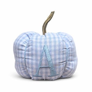 May include: A fabric pumpkin decoration featuring a light blue and white gingham check pattern. The center of the pumpkin is embroidered with a large, metallic light blue letter A. A brown, textured stem extends from the top of the round pumpkin.