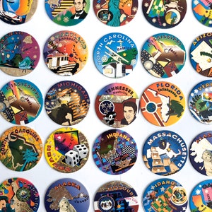 May include: A collection of 25 round, colourful, state-themed tokens. Each token features a state name, a city name, and a graphic design representing the state. The tokens are arranged in a grid pattern on a white background.
