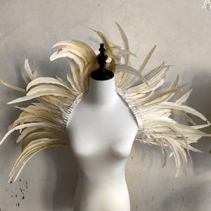 May include: A white feather shoulder piece on a white mannequin. The feathers are arranged in a circular shape around the shoulders.