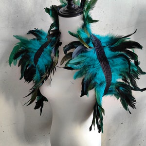 Puede incluir: Un collar de boa de plumas de color azul verdoso y negro. La boa está hecha de plumas suaves y es perfecta para añadir un toque de glamour a cualquier atuendo.