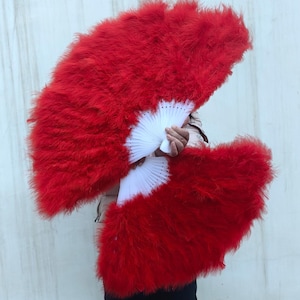 May include: Two large, vibrant red feather fans with white folding bases. The fans are held open, showcasing the bright red feathers and the contrasting white base. The fans are a striking accessory.
