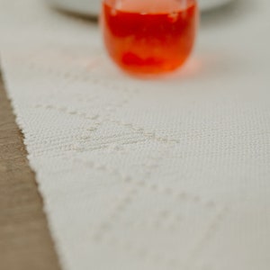 K&ouml;nnte beinhalten: Ein Glas mit rotem Saft steht auf einem wei&szlig;en Tischl&auml;ufer mit einem zarten Muster. Das Glas ist klar und hat einen abgerundeten Boden.
