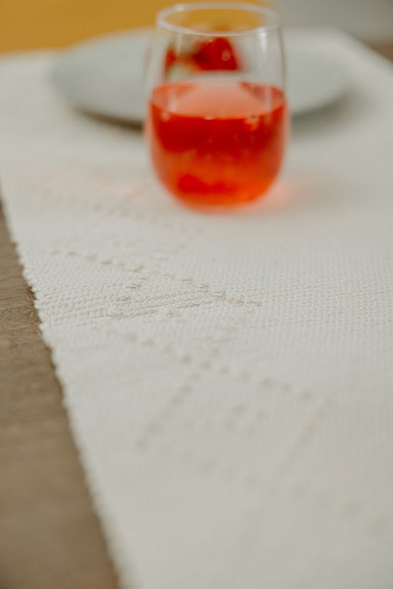 K&ouml;nnte beinhalten: Ein Glas mit rotem Saft steht auf einem wei&szlig;en Tischl&auml;ufer mit einem zarten Muster. Das Glas ist klar und hat einen abgerundeten Boden.