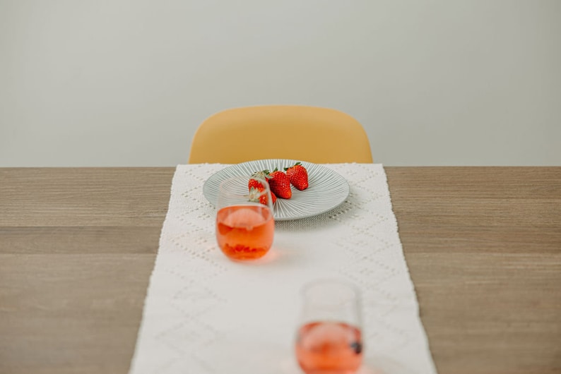 K&ouml;nnte beinhalten: Ein wei&szlig;er Tischl&auml;ufer mit einem wei&szlig;en H&auml;kelmuster, ein Teller mit drei roten Erdbeeren und zwei klare Gl&auml;ser gef&uuml;llt mit einer rosa Fl&uuml;ssigkeit.