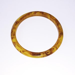 May include: A round, marbled bangle bracelet in shades of yellow and brown. The vintage-style bracelet has a smooth, glossy finish and a swirling pattern. The bangle is a classic accessory.