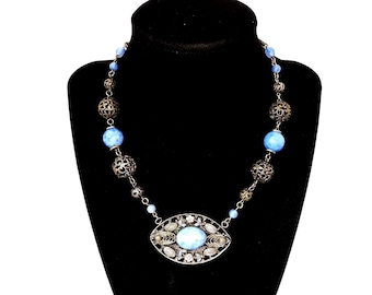 May include: A vintage necklace with a silver-tone filigree pendant and chain. The necklace features large, light blue beads and smaller silver beads. The pendant has a large, oval-shaped light blue stone surrounded by smaller clear stones.