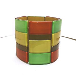 May include: A wide, colorful bracelet with rectangular segments. The bracelet features alternating rows of green, yellow, brown, and orange segments. The jewelry is made of a glossy material and is set against a white background.