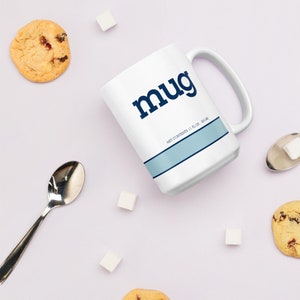 Puede incluir: Taza de cerámica blanca con la palabra "mug" en azul marino, una franja azul claro y el texto "NET CONTENTS 11 FL OZ 325 ML". La taza está rodeada de galletas, terrones de azúcar y una cuchara.