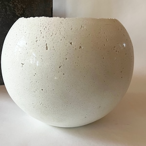 May include: A white, round, concrete planter with a rough, textured surface.