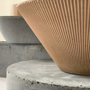 May include: A set of three concrete planters, one with a ribbed design and two with smooth surfaces. The planters are stacked on top of each other.