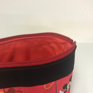 May include: Red zippered pouch with a black fabric trim. The pouch is decorated with a Mickey Mouse print featuring Mickey's head and yellow outlines.