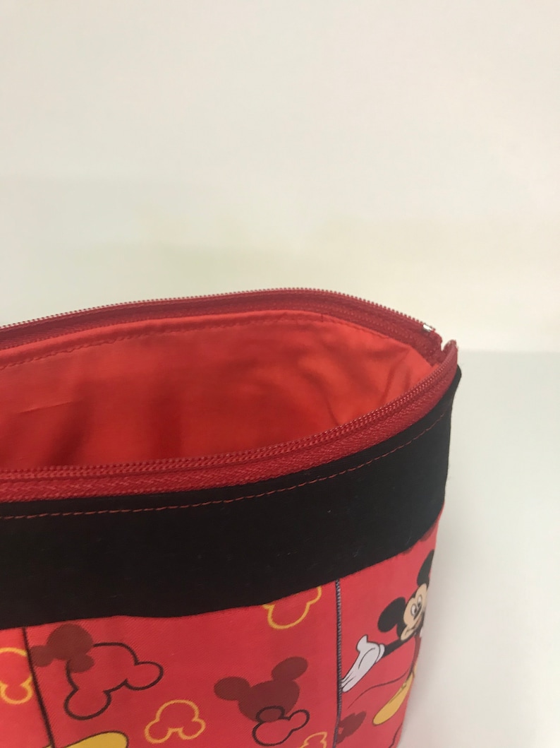 May include: Red zippered pouch with a black fabric trim. The pouch is decorated with a Mickey Mouse print featuring Mickey's head and yellow outlines.