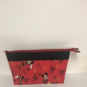 May include: Red zippered pouch with a black trim and a Mickey Mouse print. The print features Mickey Mouse in various poses with red and yellow Mickey Mouse ears.