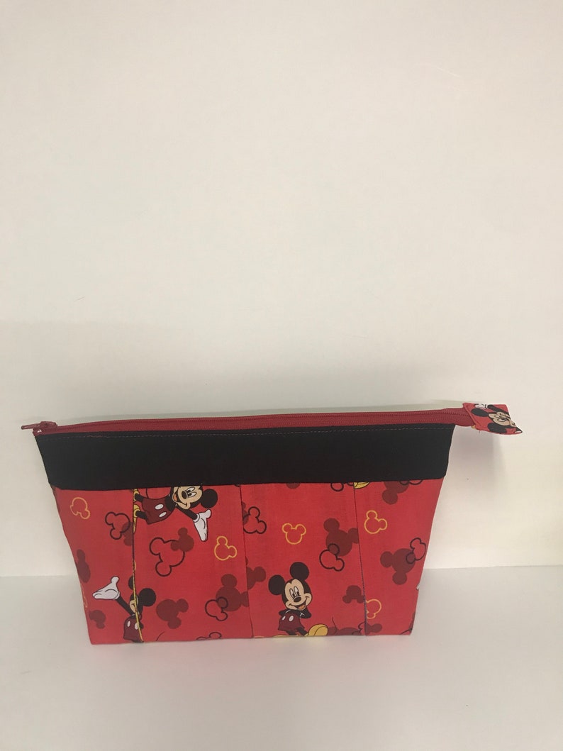 May include: Red zippered pouch with a black trim and a Mickey Mouse print. The print features Mickey Mouse in various poses with red and yellow Mickey Mouse ears.