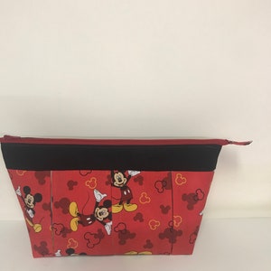 May include: Red zippered pouch with a black zipper and black trim. The pouch is decorated with a repeating pattern of Mickey Mouse in various poses on a red background with yellow Mickey Mouse ears.