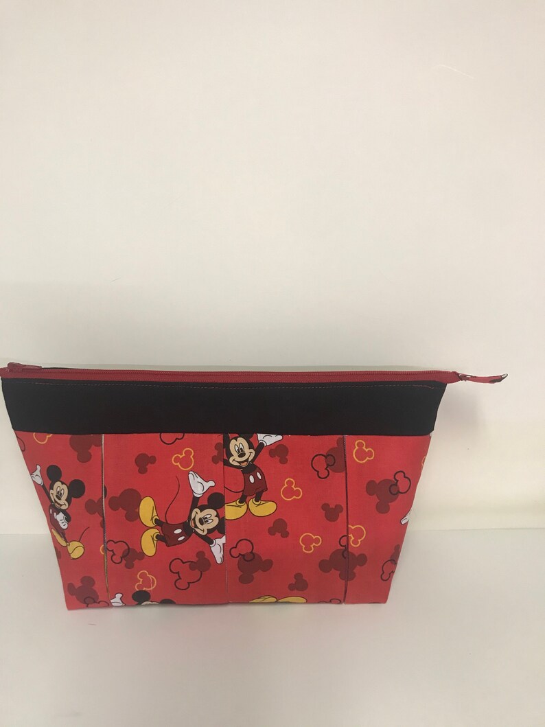 May include: Red zippered pouch with a black zipper and black trim. The pouch is decorated with a repeating pattern of Mickey Mouse in various poses on a red background with yellow Mickey Mouse ears.