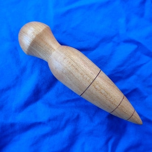 May include: A wooden tool with a rounded head and a pointed end. The tool has three dark lines running down the length of the body.
