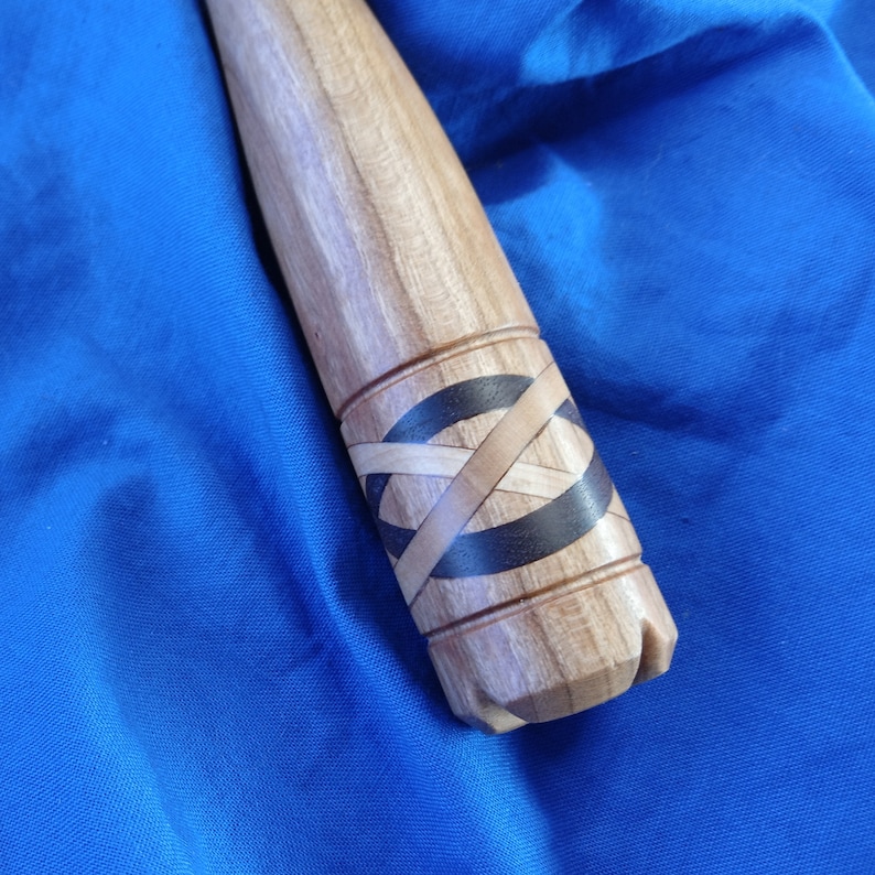 May include: Close-up of a wooden handle with a black and brown inlay design. The handle is smooth and has a rounded shape.