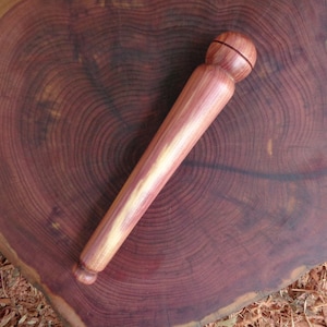 Puede incluir: Un taco de madera con un extremo redondeado, hecho de madera de cedro. El taco es de color marrón rojizo con una veta de madera natural.
