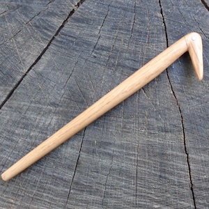 May include: A wooden knitting needle with a curved hook at the end. The needle is light brown and has a smooth finish.