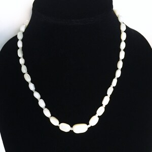 May include: A white oval-shaped bead necklace on a black velvet display stand.