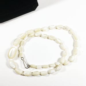 May include: A white oval-shaped bead necklace with a silver clasp. The necklace is made of smooth, polished beads.