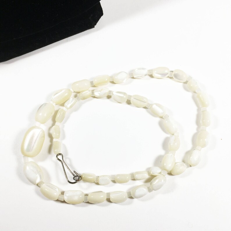 May include: A white oval-shaped bead necklace with a silver clasp. The necklace is made of smooth, polished beads.