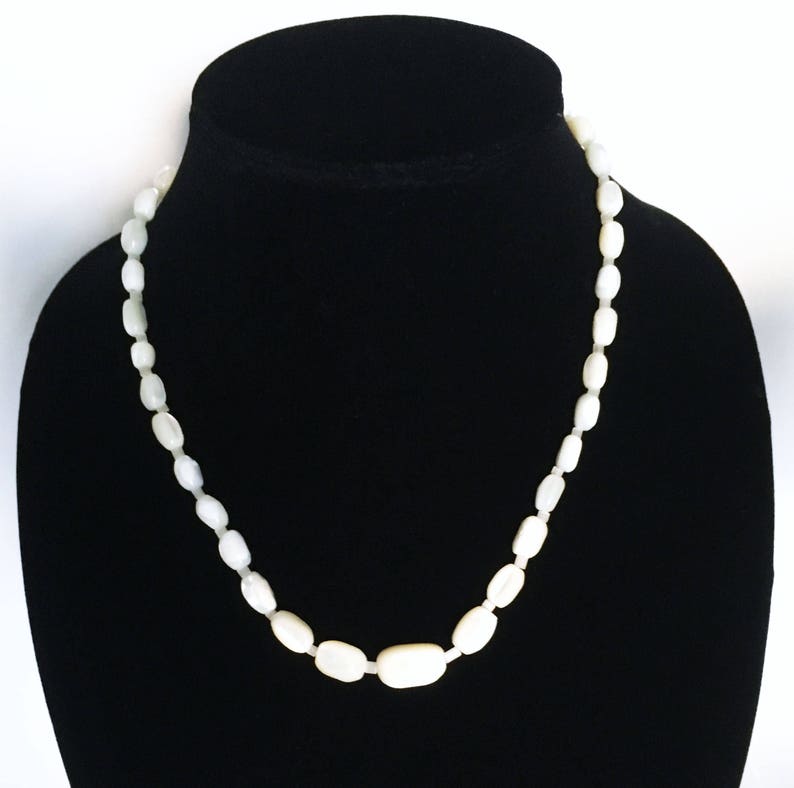May include: A white oval-shaped bead necklace on a black velvet display stand.