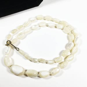 May include: A white pearl necklace with a gold clasp. The pearls are oval shaped and have a slight iridescent sheen.