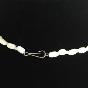 May include: A white pearl necklace with a silver clasp. The necklace is made of small, round pearls that are strung together on a thin silver chain.