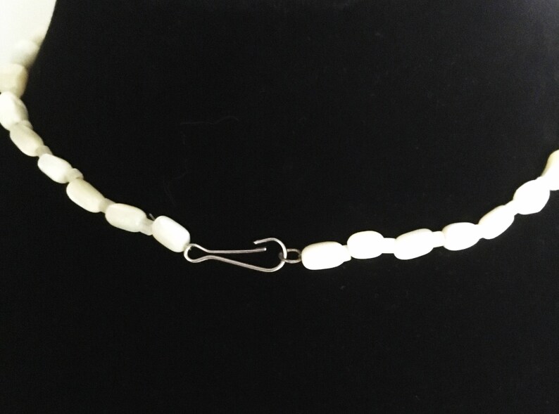 May include: A white pearl necklace with a silver clasp. The necklace is made of small, round pearls that are strung together on a thin silver chain.