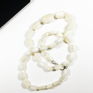 May include: A white pearl necklace with a silver clasp. The necklace is made of oval-shaped beads.