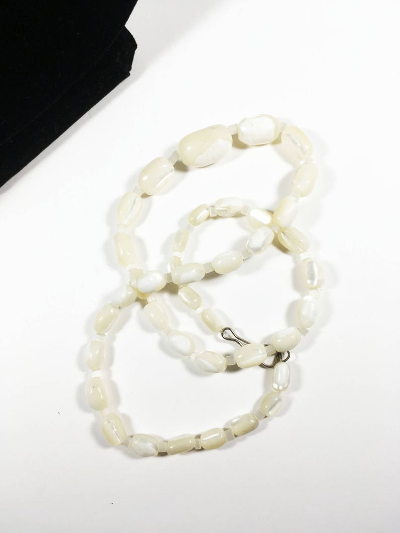 May include: A white pearl necklace with a silver clasp. The necklace is made of oval-shaped beads.