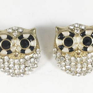 May include: A pair of gold owl stud earrings with black and white enamel detailing and clear rhinestones.