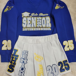 May include: A royal blue sweatshirt with the text "Jada Brown Senior 2025 Lofton High School" and a white pleated skirt with the text "Senior Class of 2025 LHS" in blue and yellow glitter.
