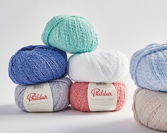 Könnte beinhalten: Sechs Knäuel Garn in verschiedenen Farben, darunter Blau, Weiß, Rosa und Beige. Das Garn ist mit "Phildar" und "PHL BABY DOLL" gekennzeichnet.