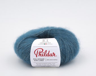 May include: A ball of teal Phil Mohair Soie Lurex yarn. The yarn has a soft, fluffy texture and a label with the brand name and product details. The label also states the yarn is made in Italy.