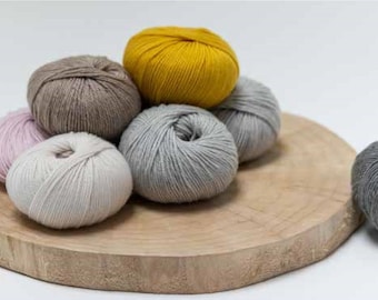 May include: A collection of six yarn balls in various colors, including pink, beige, gray, and yellow, arranged on a wooden surface.