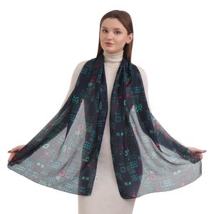 May include: A black sheer scarf with a geometric pattern in shades of green and red. The scarf is draped around a person's neck.