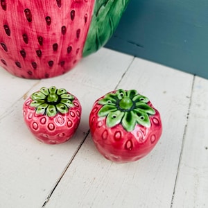 Puede incluir: Dos saleros y pimenteros de cerámica en forma de fresa roja y verde. Los saleros están detallados con hojas verdes y semillas blancas.