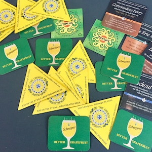 May include: A collection of green and yellow coasters with the text "The Church Brew Works" and "Schweppes Bitter Grapefruit". The coasters are on a dark gray surface.