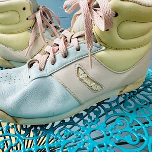 May include: A pair of light blue, pink and yellow high-top trainers with pink laces. The trainers have a white sole and the text "Boss Air" on the side.