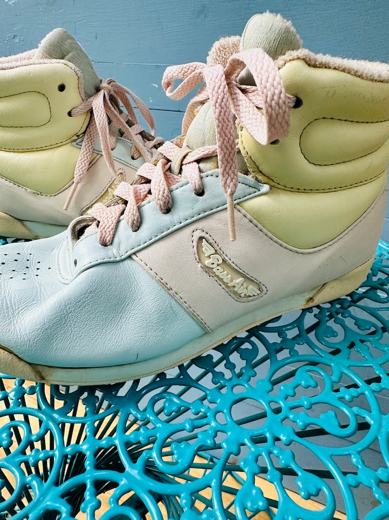 May include: A pair of light blue, pink and yellow high-top trainers with pink laces. The trainers have a white sole and the text "Boss Air" on the side.