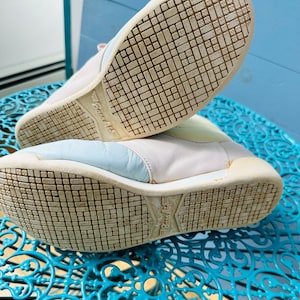 May include: A pair of white leather trainers with blue and yellow accents. The trainers have a textured sole with the word "Bounce Air" printed on the bottom.